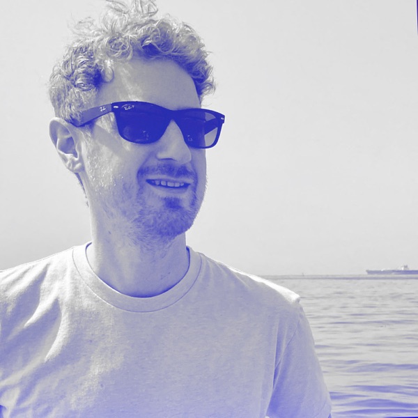 Alex Camp, smiling in sunglasses by the ocean